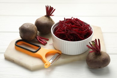 Photo of Raw beetroot noodles, fresh vegetables and peeler on white wooden table, closeup. Vegetarian dish