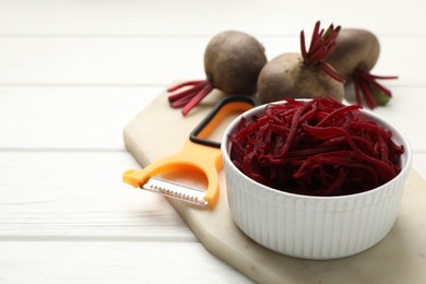 Photo of Raw beetroot noodles, fresh vegetables and peeler on white wooden table, closeup. Space for text