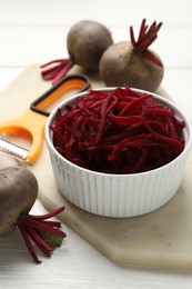 Photo of Raw beetroot noodles, fresh vegetables and peeler on white wooden table, closeup. Vegetarian dish