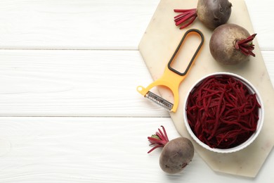 Photo of Raw beetroot noodles, fresh vegetables and peeler on white wooden table, flat lay. Space for text