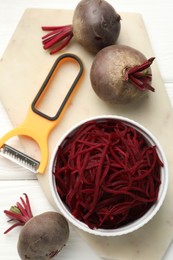 Photo of Raw beetroot noodles, fresh vegetables and peeler on white wooden table, flat lay