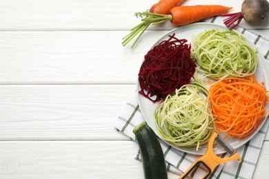 Photo of Vegetarian dish. Different vegetable noodles, fresh vegetables and peeler on white wooden table, flat lay. Space for text