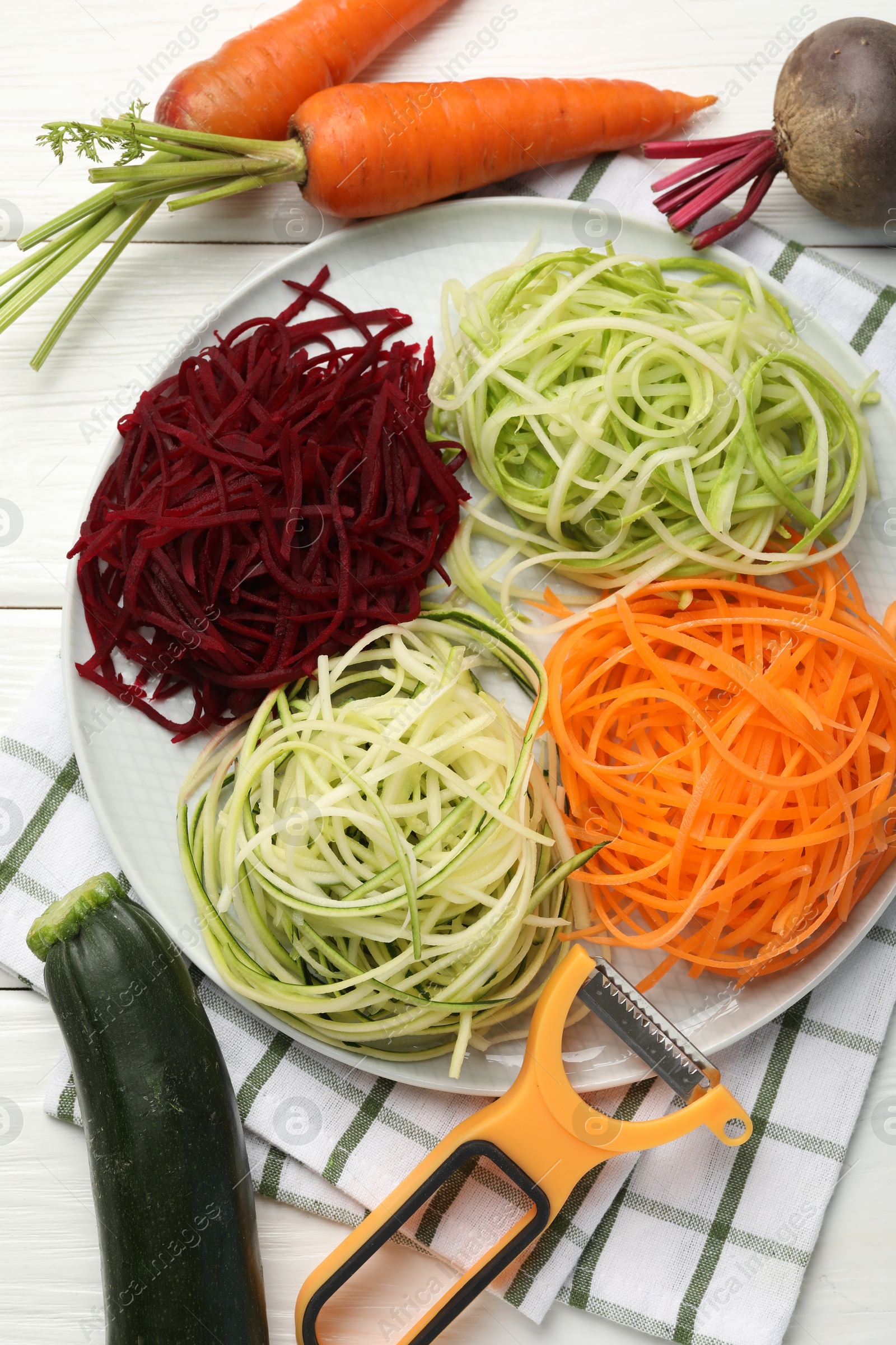 Different vegetable noodles, fresh vegetables and peeler on white wooden table, flat lay. Vegetarian dish Photo of Different vegetable noodles, fresh vegetables and peeler on white wooden table, flat lay. Vegetarian dish