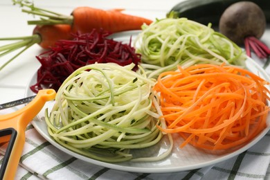 Photo of Different vegetable noodles, fresh vegetables and peeler on table, closeup. Vegetarian dish
