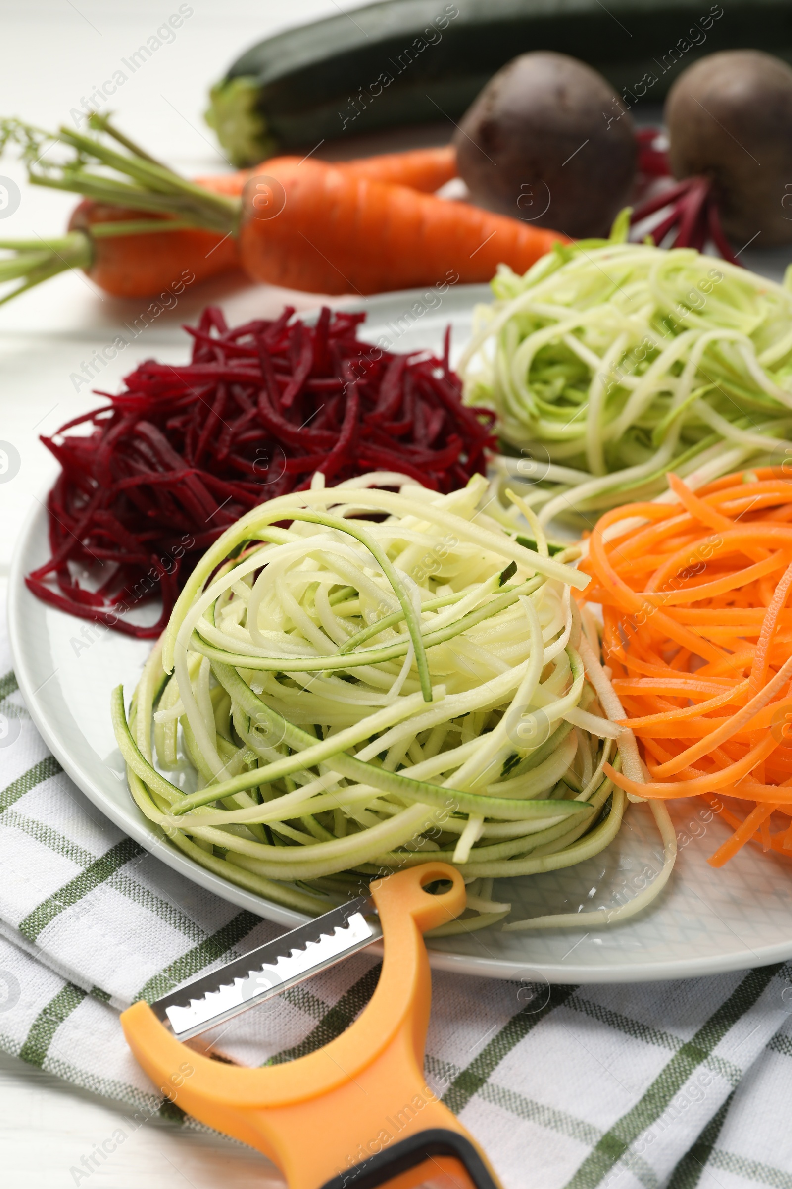 Photo of Different vegetable noodles, fresh vegetables and peeler on table, closeup. Vegetarian dish