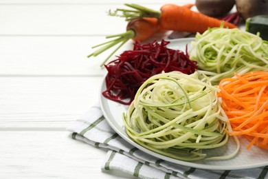 Photo of Vegetarian dish. Different vegetable noodles and fresh vegetables on white wooden table, closeup. Space for text