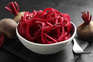 Photo of Raw beetroot noodles and fresh vegetables on black table, closeup. Vegetarian dish