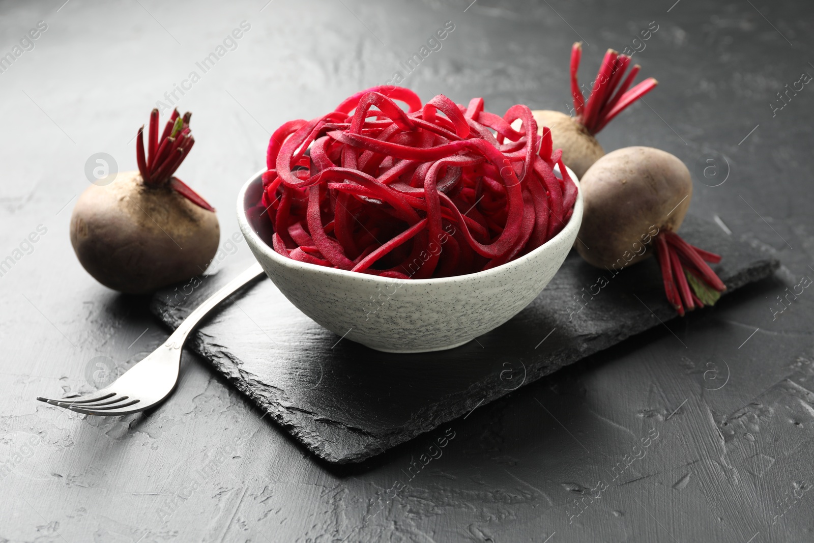 Raw beetroot noodles and fresh vegetables on black table, closeup. Vegetarian dish Photo of Raw beetroot noodles and fresh vegetables on black table, closeup. Vegetarian dish