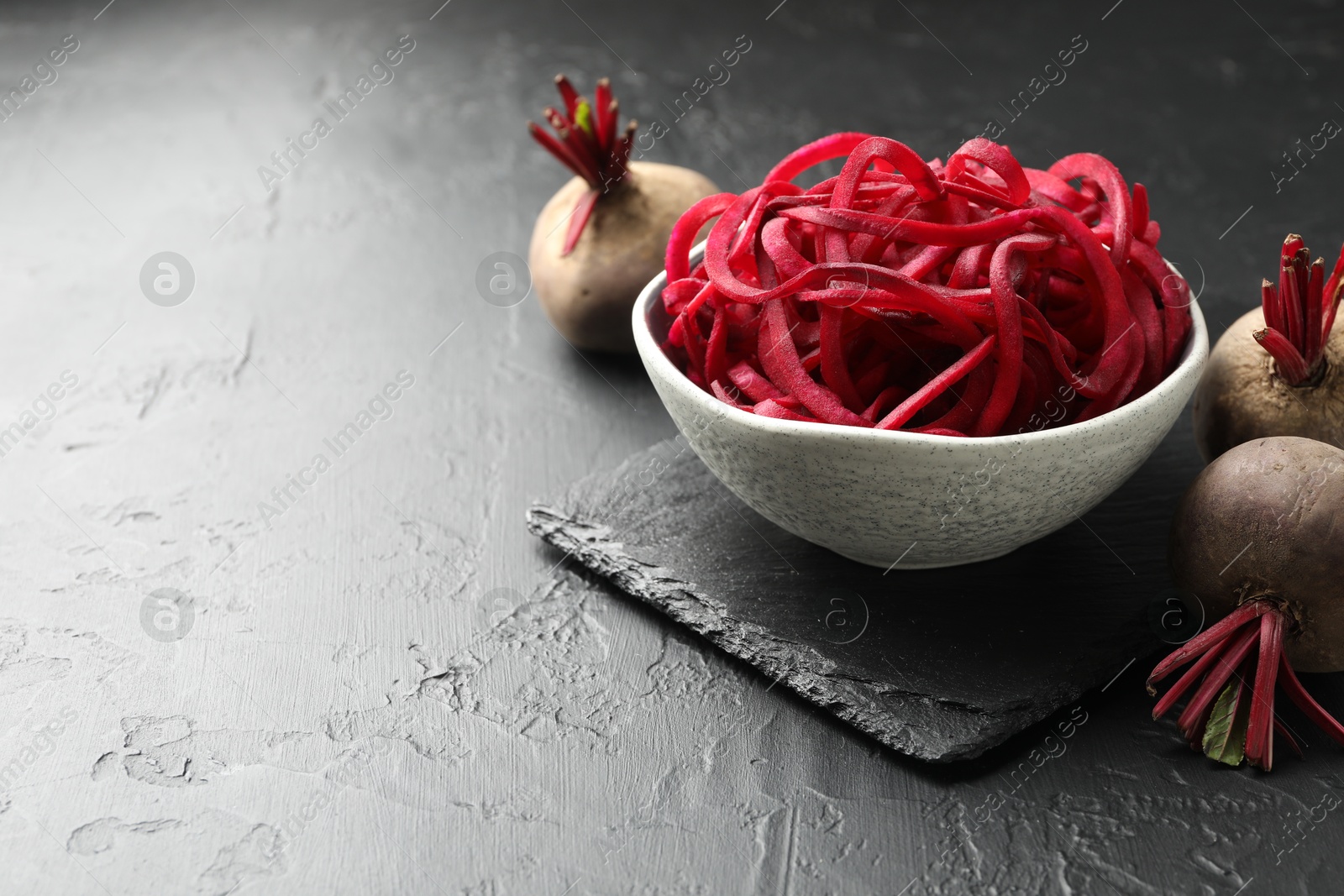 Vegetarian dish. Raw beetroot noodles and fresh vegetables on black table, closeup. Space for text Photo of Vegetarian dish. Raw beetroot noodles and fresh vegetables on black table, closeup. Space for text