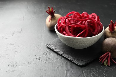 Photo of Vegetarian dish. Raw beetroot noodles and fresh vegetables on black table, closeup. Space for text
