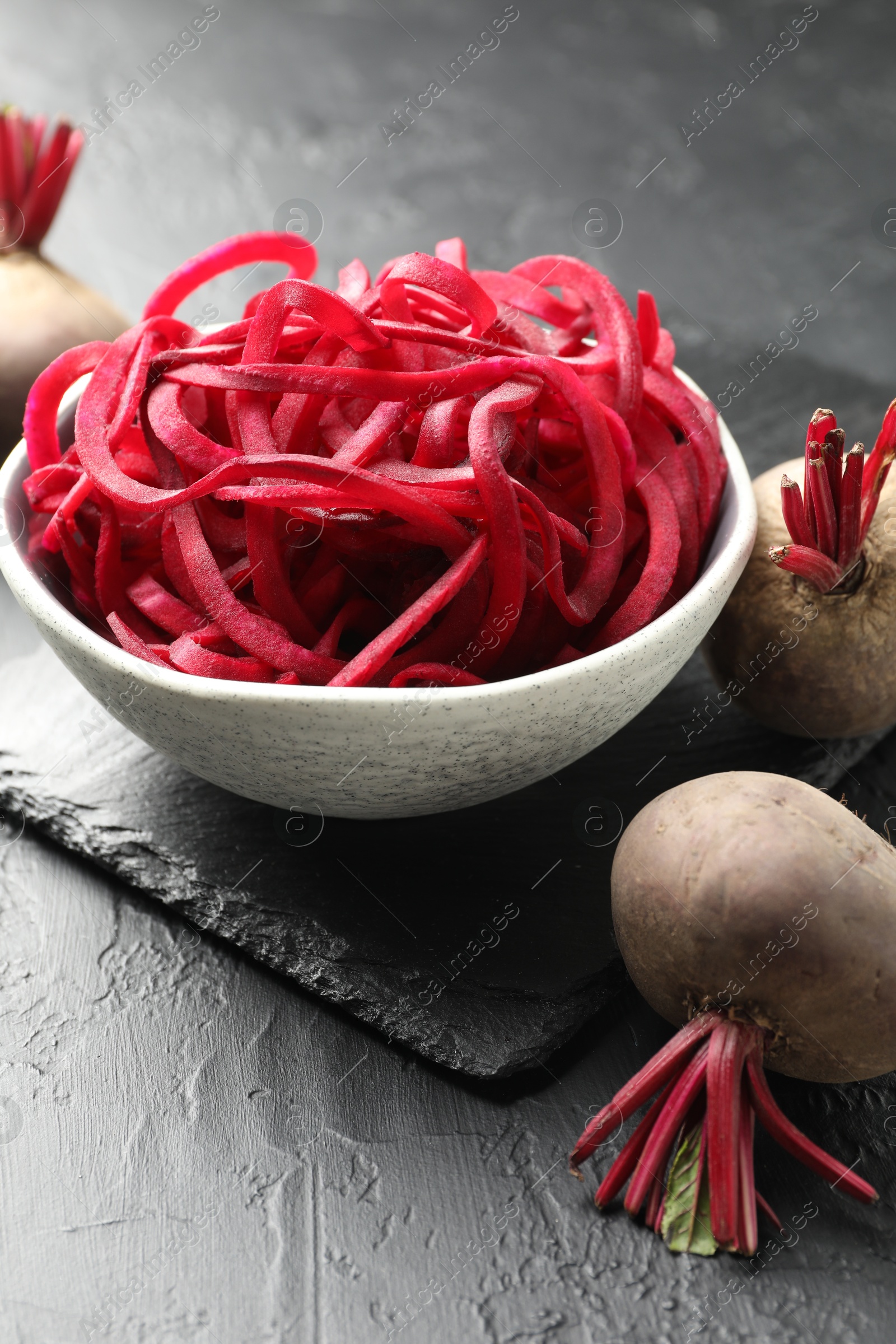 Photo of Raw beetroot noodles and fresh vegetables on black table, closeup. Vegetarian dish