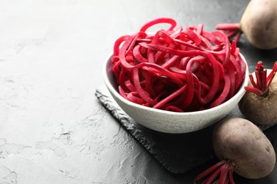 Photo of Vegetarian dish. Raw beetroot noodles and fresh vegetables on black table, closeup. Space for text