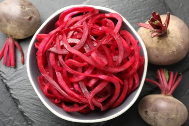 Photo of Raw beetroot noodles and fresh vegetables on black table, flat lay. Vegetarian dish