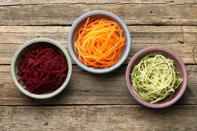 Photo of Different vegetable noodles in bowls on wooden table, flat lay. Vegetarian dish
