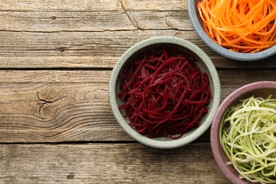 Photo of Vegetarian dish. Different vegetable noodles in bowls on wooden table, flat lay. Space for text