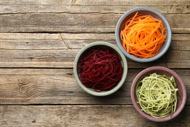 Photo of Vegetarian dish. Different vegetable noodles in bowls on wooden table, flat lay. Space for text