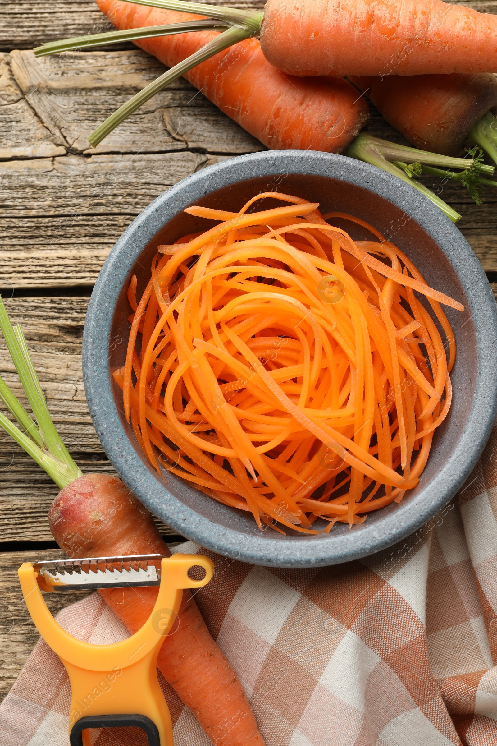 Photo of Raw beetroot noodles, fresh vegetables and peeler on wooden table, flat lay. Vegetarian dish