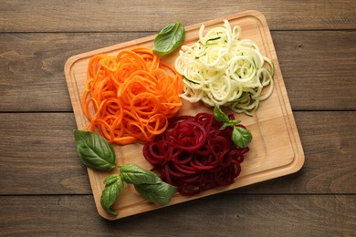 Photo of Different vegetable noodles with basil on wooden table, top view. Vegetarian dish