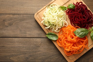 Photo of Vegetarian dish. Different vegetable noodles with basil on wooden table, top view. Space for text