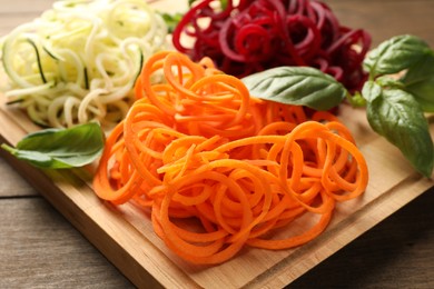 Photo of Different vegetable noodles with basil on wooden table, closeup. Vegetarian dish