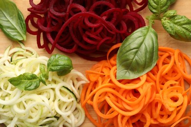 Photo of Different vegetable noodles with basil on wooden table, flat lay. Vegetarian dish