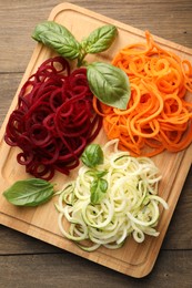 Photo of Different vegetable noodles with basil on wooden table, top view. Vegetarian dish