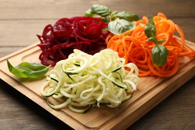 Photo of Different vegetable noodles with basil on wooden table, closeup. Vegetarian dish