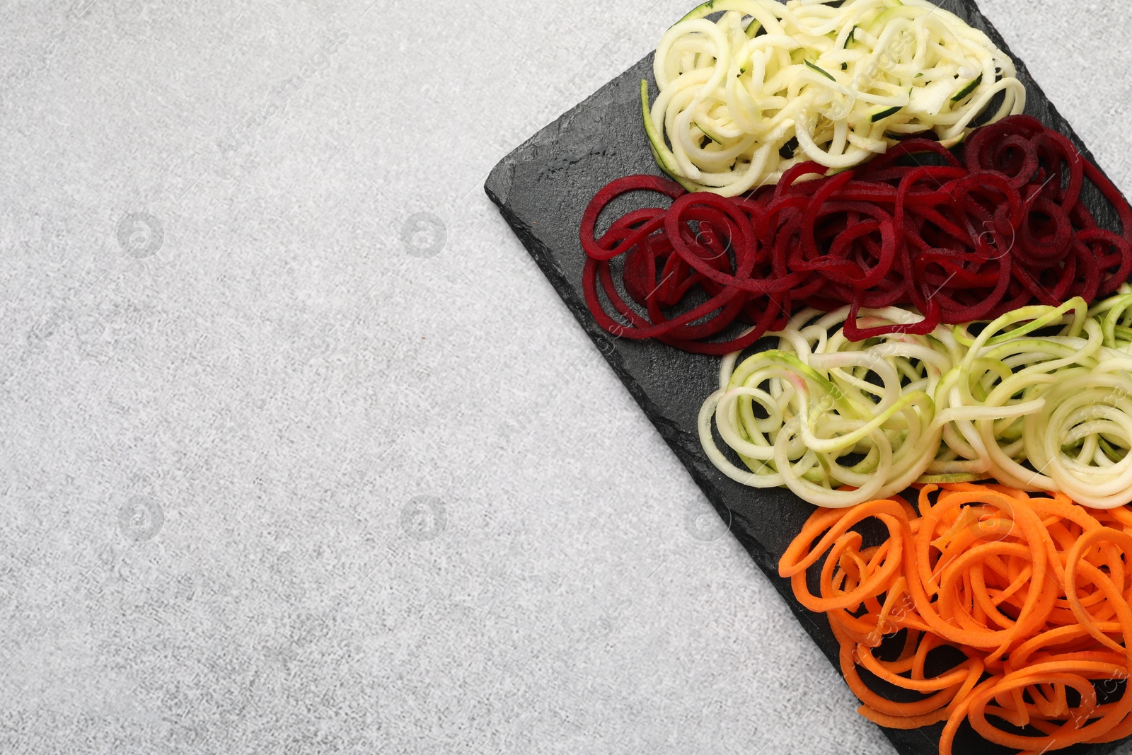 Photo of Vegetarian dish. Different vegetable noodles on grey table, top view. Space for text