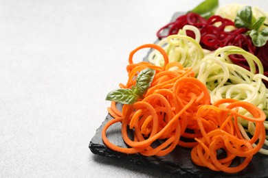Photo of Vegetarian dish. Different vegetable noodles with basil on grey table, closeup. Space for text