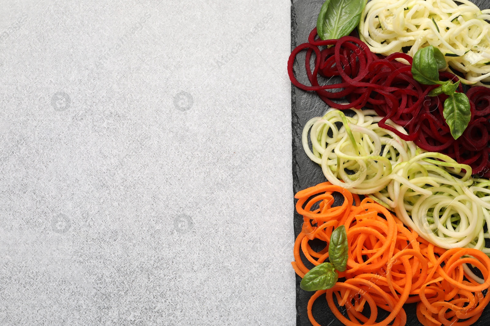 Photo of Vegetarian dish. Different vegetable noodles with basil on grey table, top view. Space for text