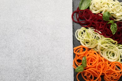Photo of Vegetarian dish. Different vegetable noodles with basil on grey table, top view. Space for text