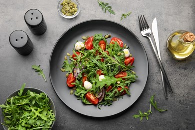 Photo of Tasty salad with arugula, mozzarella and vegetables served on grey table, flat lay