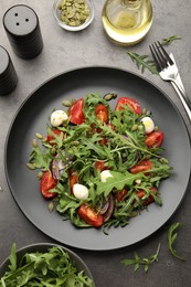 Photo of Tasty salad with arugula, mozzarella and vegetables served on grey table, flat lay
