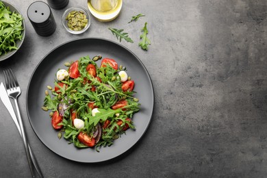 Photo of Tasty salad with arugula, mozzarella and vegetables served on grey table, flat lay. Space for text