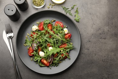 Photo of Tasty salad with arugula, mozzarella and vegetables served on grey table, flat lay. Space for text