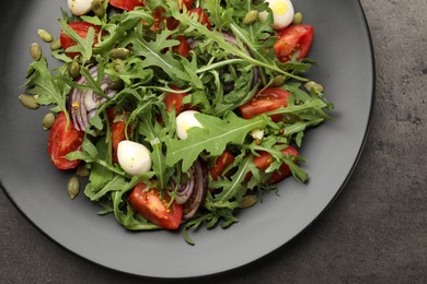 Photo of Tasty salad with arugula, mozzarella and vegetables on grey table, top view
