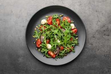Photo of Tasty salad with arugula, mozzarella and vegetables on grey table, top view