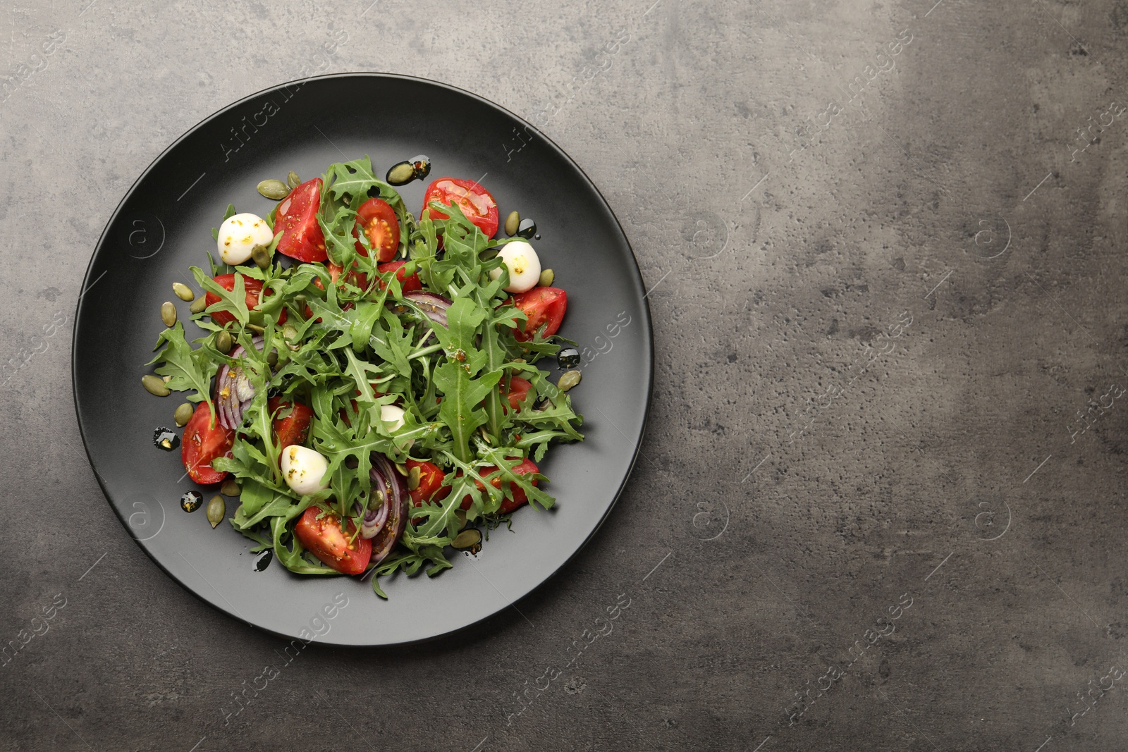Tasty salad with arugula, mozzarella and vegetables on grey table, top view. Space for text Photo of Tasty salad with arugula, mozzarella and vegetables on grey table, top view. Space for text