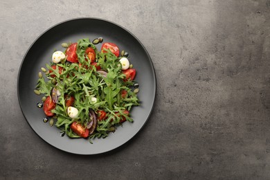 Photo of Tasty salad with arugula, mozzarella and vegetables on grey table, top view. Space for text