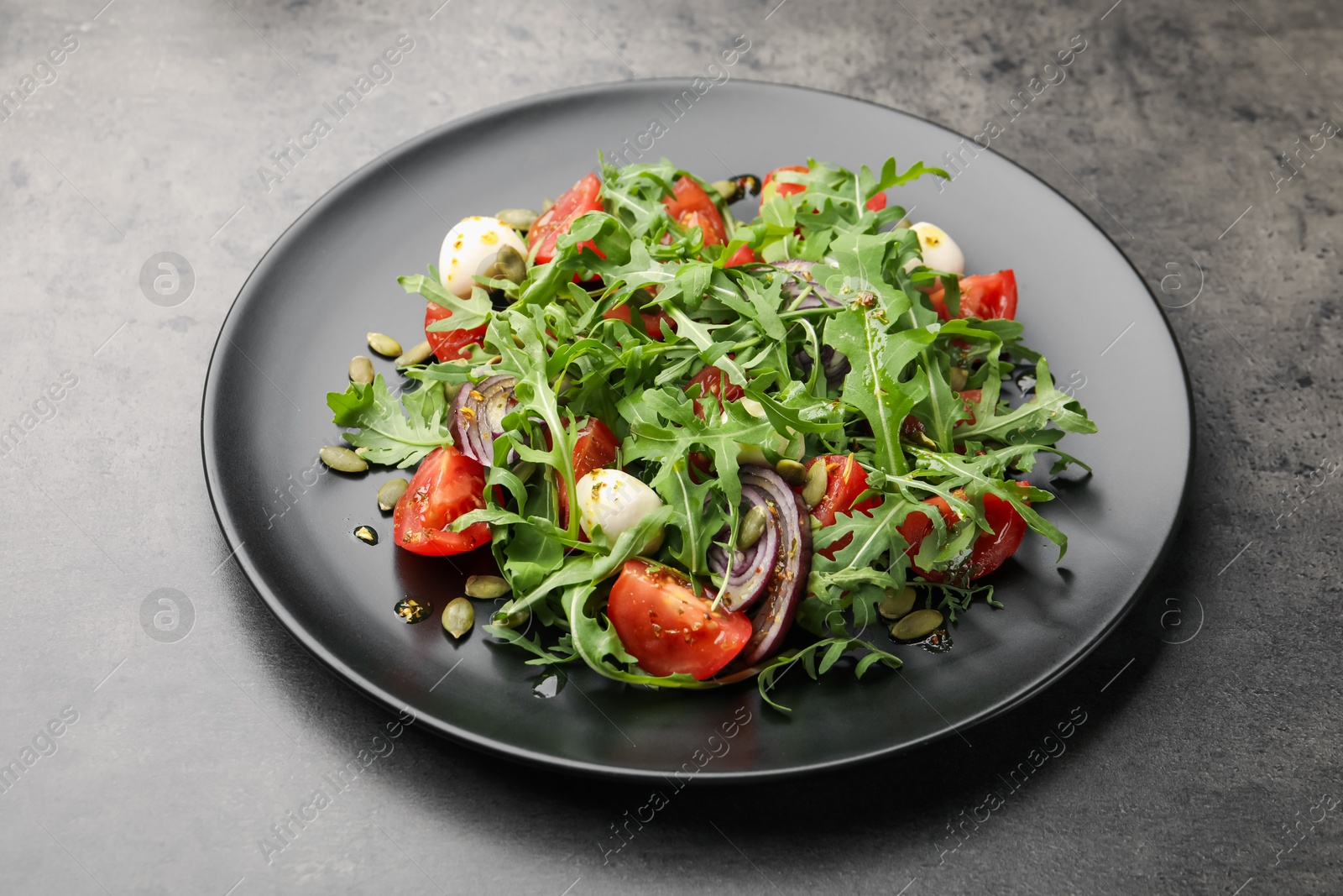 Tasty salad with arugula, mozzarella and vegetables on grey table, closeup Photo of Tasty salad with arugula, mozzarella and vegetables on grey table, closeup