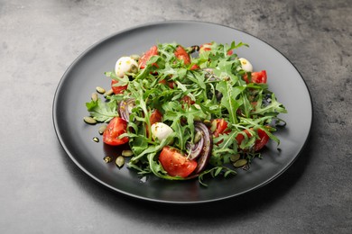 Photo of Tasty salad with arugula, mozzarella and vegetables on grey table, closeup
