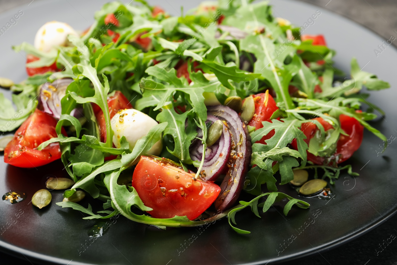 Tasty salad with arugula, mozzarella and vegetables on table, closeup Photo of Tasty salad with arugula, mozzarella and vegetables on table, closeup