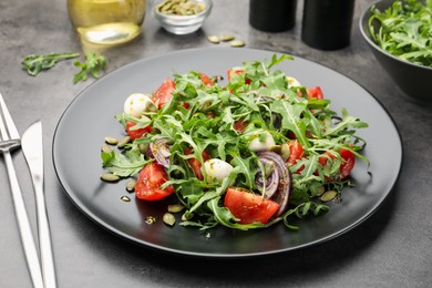 Photo of Tasty salad with arugula, mozzarella and vegetables served on grey table, closeup