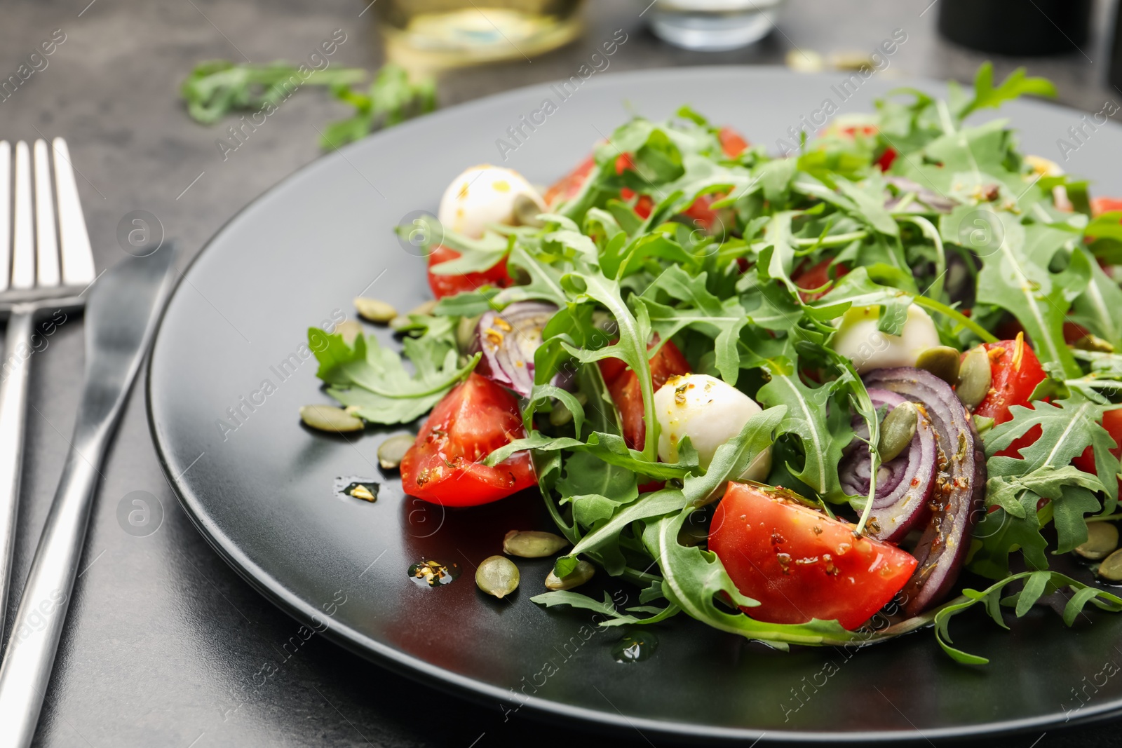 Tasty salad with arugula, mozzarella and vegetables served on grey table, closeup Photo of Tasty salad with arugula, mozzarella and vegetables served on grey table, closeup
