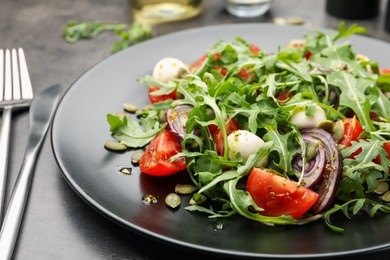 Photo of Tasty salad with arugula, mozzarella and vegetables served on grey table, closeup