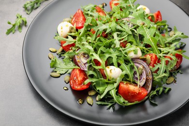 Photo of Tasty salad with arugula, mozzarella and vegetables on grey table, closeup