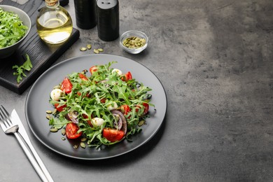 Photo of Tasty salad with arugula, mozzarella and vegetables served on grey table, closeup. Space for text