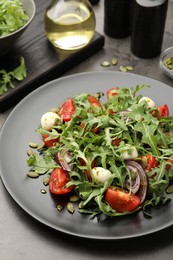 Photo of Tasty salad with arugula, mozzarella and vegetables served on grey table, closeup