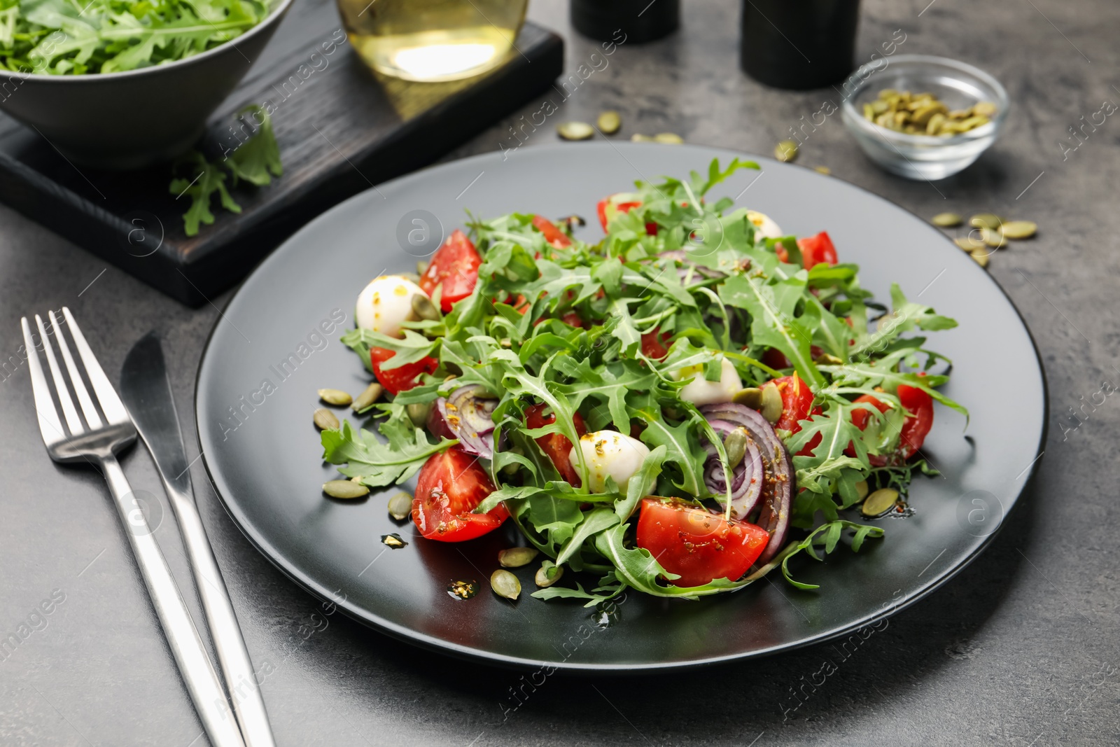 Tasty salad with arugula, mozzarella and vegetables served on grey table, closeup Photo of Tasty salad with arugula, mozzarella and vegetables served on grey table, closeup