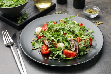 Photo of Tasty salad with arugula, mozzarella and vegetables served on grey table, closeup
